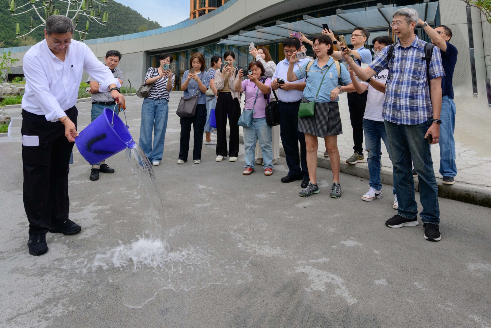 張安平親自拿水桶倒水,示範以營建廢棄物製成的透水混凝土道路,吸水能力明顯，能減緩熱島效應因應極端氣候